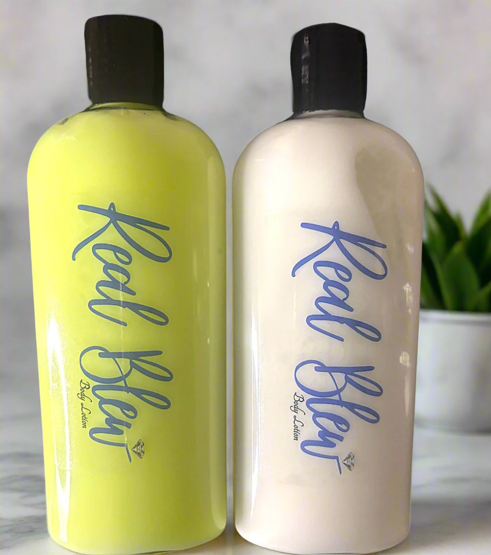 Two bottles with pump dispensers are placed side by side against a marble background with a plant in the background. The bottle on the left is filled with a yellow substance and has “Real Shea” written in red cursive script, followed by smaller text underneath. The bottle on the right contains a white substance and also has “Real Shea” written in blue cursive script, with similar smaller text beneath it. Both bottles have black caps and labels that suggest they contain shea-based products.